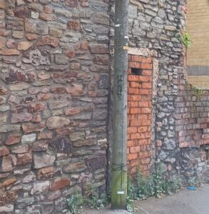 Images show two views of the end wall of a building where a doorway has been blocked out. One brick is missing, rather like a posting or spy hole has been left.